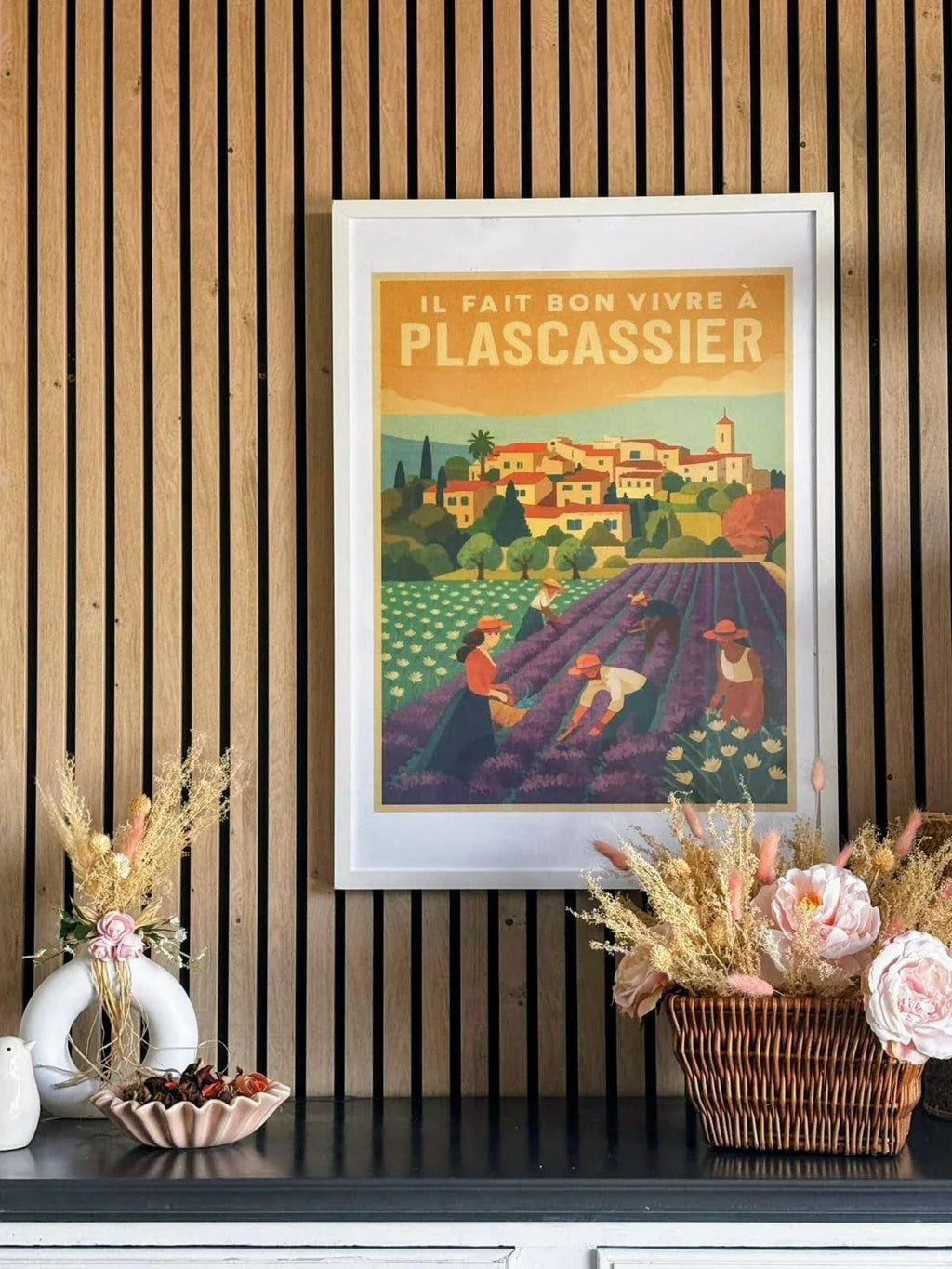 Affiche rétro 'Il Fait Bon Vivre à Plascassier' encadrée dans un décor intérieur avec fleurs.